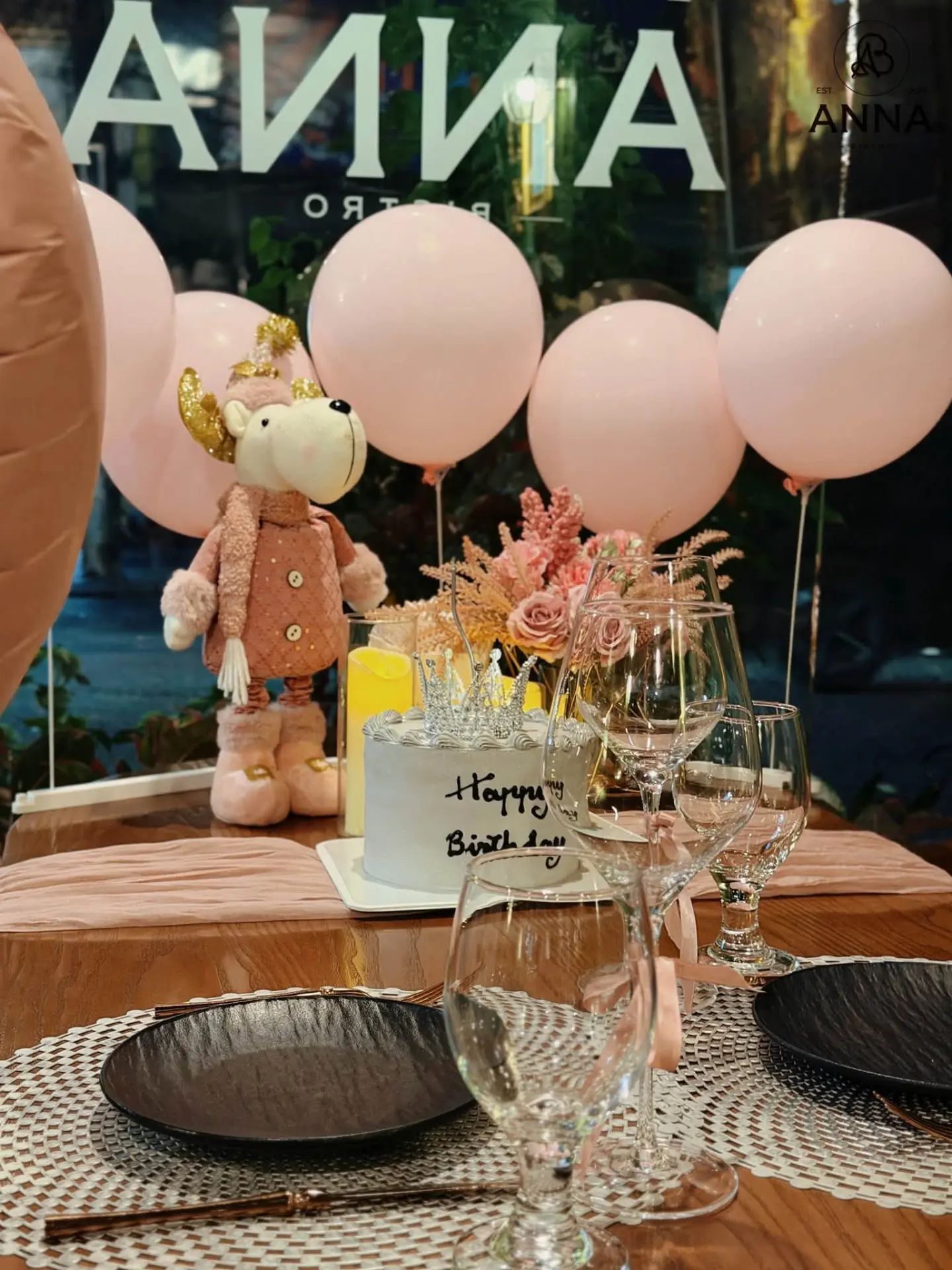 Bàn tiệc sinh nhật tại Anna's Bistro với bánh kem, bóng bay hồng và ly rượu