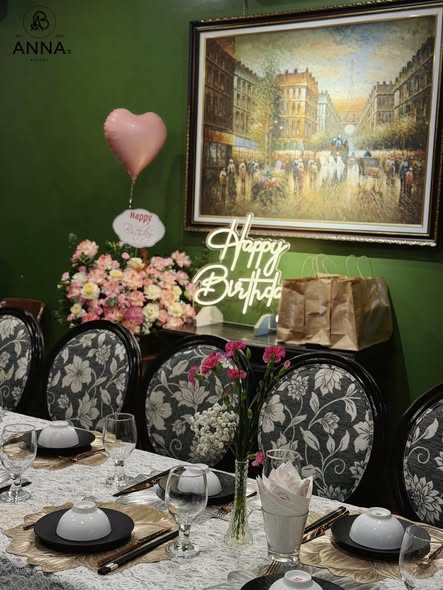 Bàn tiệc sinh nhật trong phòng tường xanh với đèn neon và hoa tươi tại Anna's Bistro